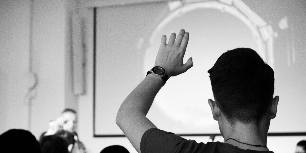 Ein Teilnehmer sitzt in einem Publikum von Anja Förster und hebt die Hand.