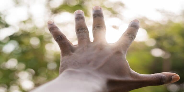 Offene Hand mit gespreizten Fingern vor verschwommenem, grünem Hintergrund im Sonnenlicht